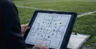 Træner med taktiktavle på tablet ved fodboldbanen